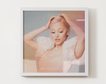 May include: A framed print featuring a woman with light pink hair, wearing a light pink top. The image has a soft, dreamy aesthetic with a blurred background and text at the bottom. The woman is touching her hair.