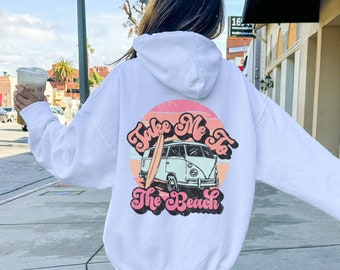 May include: White hooded sweatshirt with a pink and orange graphic on the back. The graphic features a vintage van with a surfboard on top and the text "Take Me To The Beach".