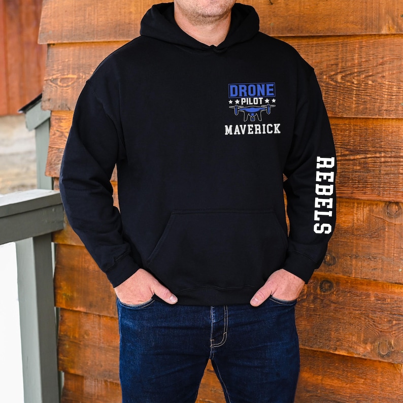 May include: Black hoodie with a front pocket and a hood. The front features the text "DRONE PILOT" above a drone graphic and the word "MAVERICK". The right sleeve has the word "REBELS" printed vertically in white.