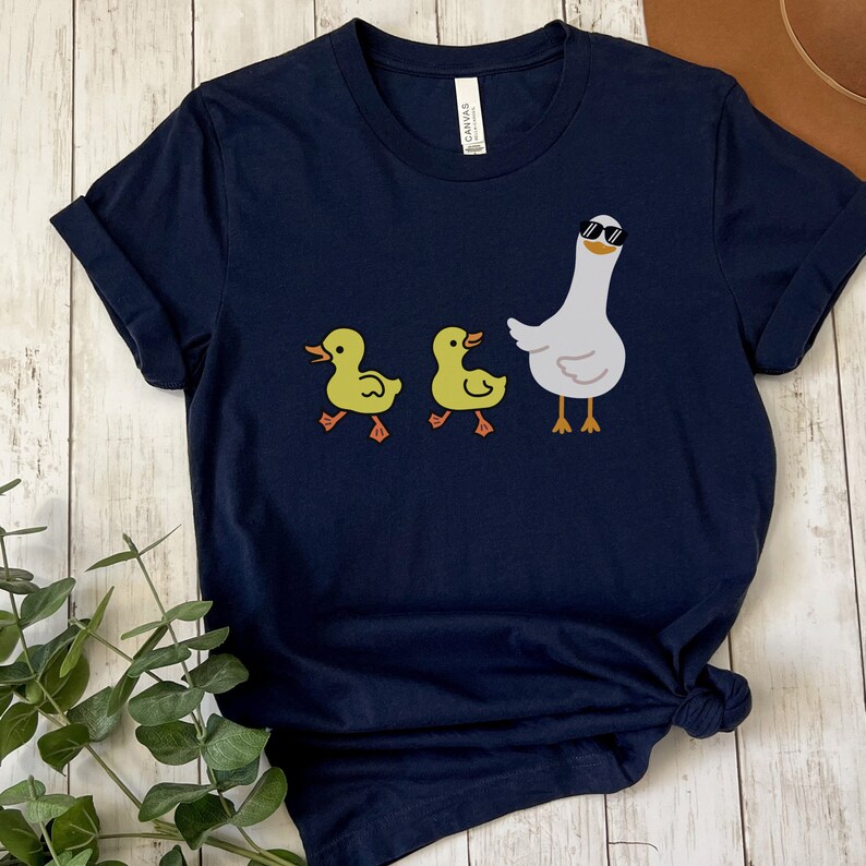 BELLA AND CANVAS T SHIRT WITH A CUTE DESIGN OF TWO DUCKS AND THEN A GOOSE.  AVAILABLE IN DARK GREY HEATHER, HEATHER MAUVE, NAVY, BLACK, ATHLETIC HEATHER AND HEATHER SLATE.