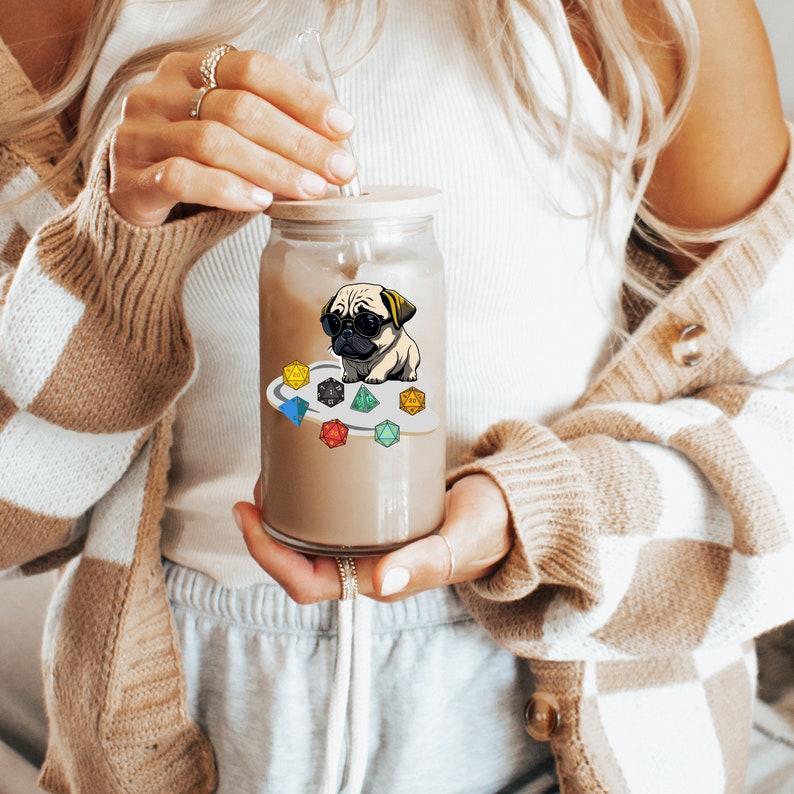 May include: A clear glass jar with a brown lid and a brown liquid inside. The jar has a sticker of a pug wearing sunglasses and sitting on a circle of colorful dice.