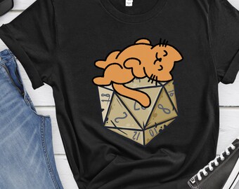 May include: Black t-shirt with a cartoon orange cat sleeping on top of a brown 20-sided die.