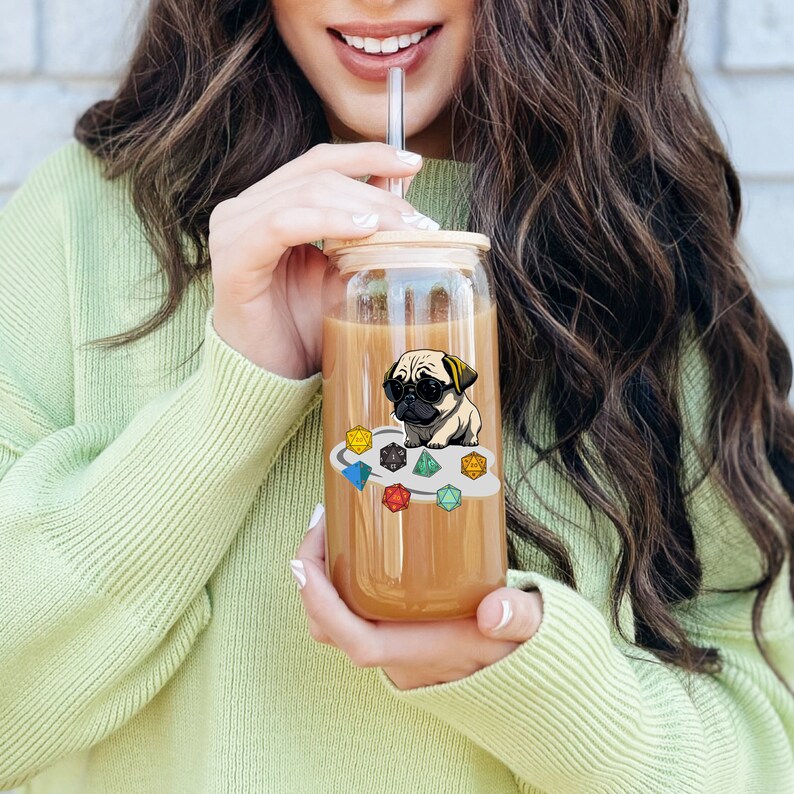 May include: A clear glass tumbler with a bamboo lid and a colorful sticker of a pug wearing sunglasses and sitting on a cloud of dice. The tumbler is filled with a brown liquid.