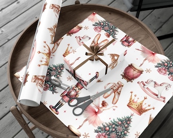May include: White wrapping paper with a ballet-themed design featuring crowns, ballet shoes, ballerinas, Christmas trees, and nutcrackers. A wrapped gift with a brown ribbon and scissors are on the paper. A roll of the same paper is on the left.
