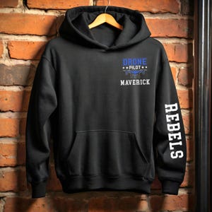 May include: Black hoodie with a front pocket and a hood. The front features the text "DRONE PILOT" above a drone graphic and the word "MAVERICK". The right sleeve has the word "REBELS" printed vertically in white.