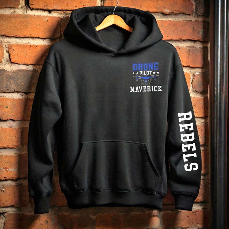 May include: Black hoodie with a front pocket and a hood. The front features the text "DRONE PILOT" above a drone graphic and the word "MAVERICK". The right sleeve has the word "REBELS" printed vertically in white.