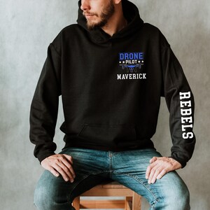 May include: Black hoodie with a front pocket and a blue and white graphic that reads "DRONE PILOT" above a drone illustration and the word "MAVERICK". The right sleeve has the word "REBELS" in white.