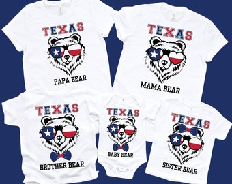 May include: White t-shirts with a Texas bear design. Each shirt features a bear face wearing sunglasses with the Texas flag design. Text on the shirts reads "PAPA BEAR", "MAMA BEAR", "BROTHER BEAR", "BABY BEAR", and "SISTER BEAR".