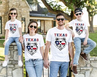 May include: Four people wearing white t-shirts with a Texas-themed bear graphic and the text "TEXAS family vacation." The bear graphic features sunglasses with the Texas flag design. They are wearing sunglasses and jeans.