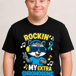 Op de afbeelding: Zwart t-shirt met een afbeelding van een wasbeer met een zonnebril en een koptelefoon, die een vredesteken maakt. De tekst luidt "ROCKIN' MY EXTRA CHROMOSOME" in geel en blauw, met muzieknoten en een Downsyndroom-lint.