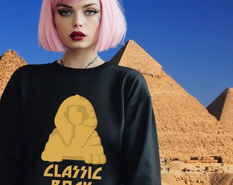 May include: Black sweatshirt with a gold Sphinx design and the words "CLASSIC ROCK." The sweatshirt is worn by a person with pink hair, set against a background of pyramids and a blue sky.