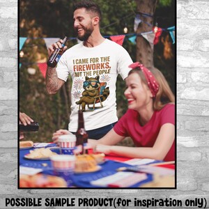 Op de afbeelding: Wit T-shirt met de tekst "I CAME FOR THE FIREWORKS, NOT THE PEOPLE" en een wasbeer met zonnebril. De wasbeer zit in een strandstoel met vuurwerk op de achtergrond. Het shirt wordt door een persoon gedragen.