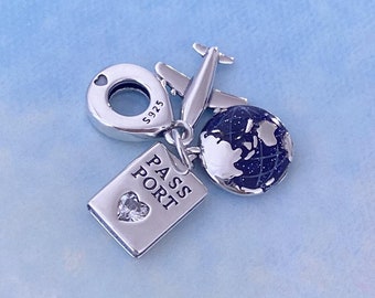 May include: Silver charm with a passport, airplane, and globe. The passport charm has the word "PASSPORT" on it and a small clear crystal heart. The airplane charm has a small silver circle with the number "S925" on it. The globe charm is blue and black with a silver outline.