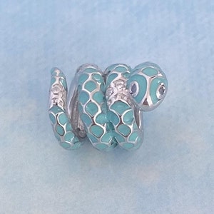 Könnte beinhalten: Ein silberner Anhänger in Form einer gewickelten türkisfarbenen Schlange mit einem weißen Steinauge.