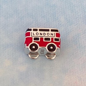 May include: A silver charm in the shape of a red double-decker bus with the word "LONDON" on the side. The charm has black wheels and a black stripe across the top.