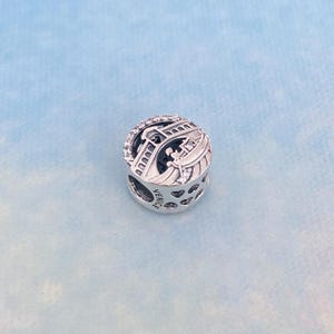 May include: Silver charm featuring a detailed depiction of the Rialto Bridge in Venice, Italy. The charm is adorned with clear cubic zirconia stones and the word "VENICE" is engraved on the side.