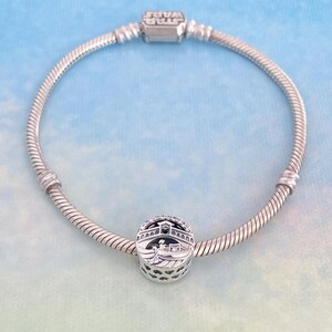 May include: A silver charm bracelet with a silver charm featuring a detailed design of a bridge with a gondola. The charm is adorned with small clear crystals.