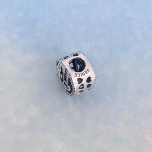 May include: Silver charm with a detailed design of a gondola and the word "VENICE" engraved on the side. The charm is decorated with small heart cutouts.
