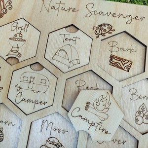 May include: Wooden nature scavenger hunt board with laser-etched illustrations and text. Features a butterfly, insect, and various hexagonal cutouts with images of a grill, tent, camper, acorn, and more. The words "Nature Scavenger Hunt" are at the top.