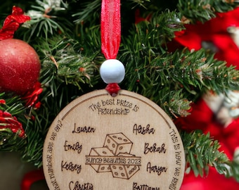 May include: A wooden Christmas ornament with the text "Bunco Beauties 2023" and the names of eight people around the edge. The ornament also features a bell and dice.