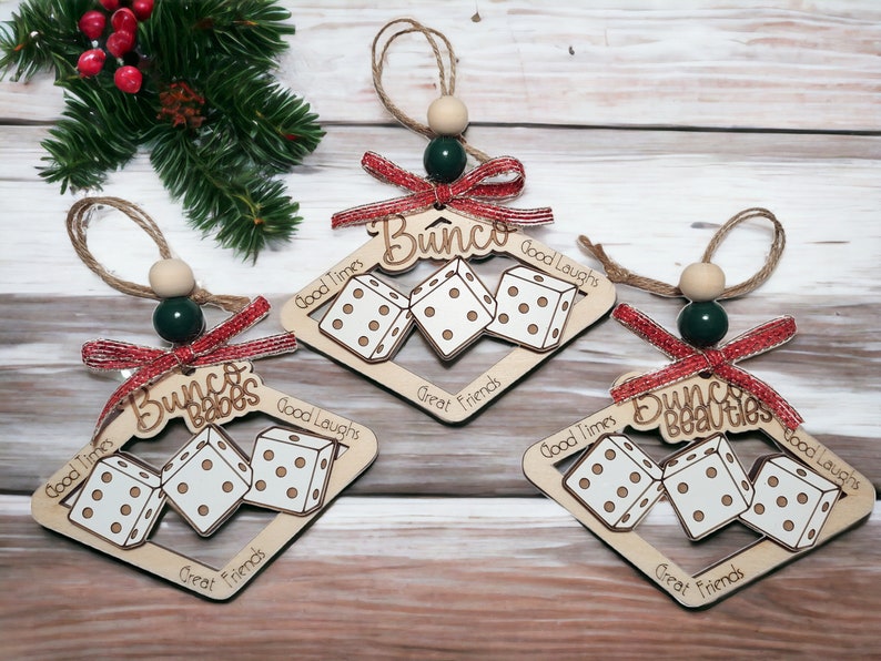 May include: Three wooden Christmas ornaments shaped like dice with the words "Bunco Babes", "Bunco" and "Bunco Beauties" written on them. Each ornament has the words "Good Times", "Good Laughs", and "Great Friends" written on it.