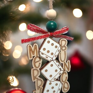 May include: A wooden Christmas bauble with a red and white bow, green and white beads, and the words "Merry Bunco" with dice hanging from the bow.