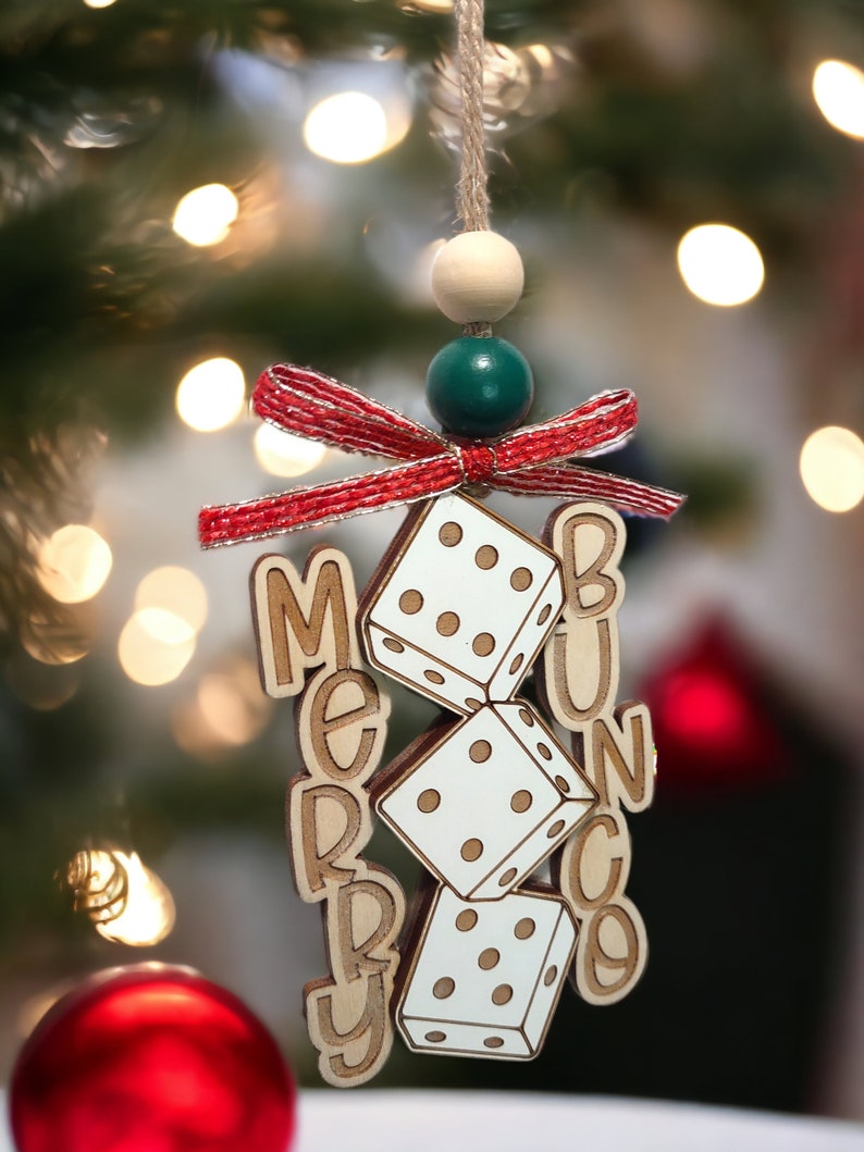 May include: A wooden Christmas bauble with a red and white bow, green and white beads, and the words "Merry Bunco" with dice hanging from the bow.
