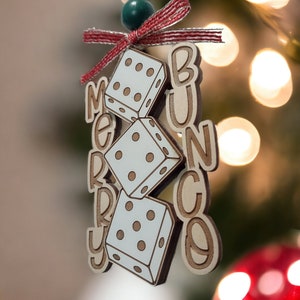 May include: A wooden Christmas bauble with the words "Merry Bunco" and three dice. The bauble is decorated with a red and white ribbon and a green bead.