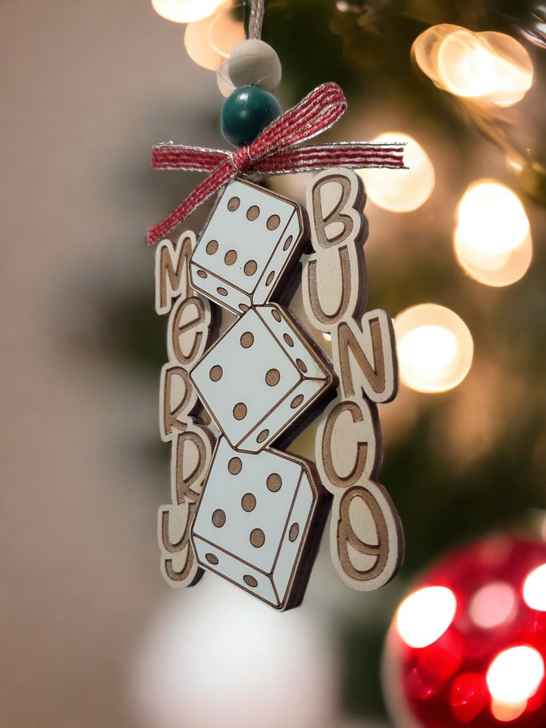 May include: A wooden Christmas bauble with the words "Merry Bunco" and three dice. The bauble is decorated with a red and white ribbon and a green bead.