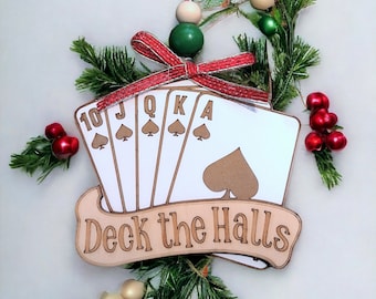 May include: Wooden Christmas ornament shaped like playing cards with the text "Deck the Halls". The cards are all spades and include the 10, Jack, Queen, King, and Ace. The ornament is decorated with a red bow and green and white beads.