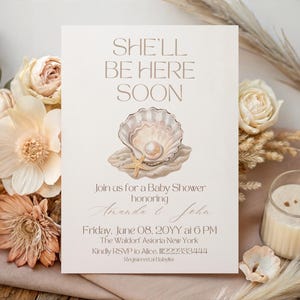 Puede incluir: Una invitación a un baby shower con el texto "SHE'LL BE HERE SOON" y detalles. El diseño presenta una concha con una perla y una estrella de mar, con detalles florales y de velas.