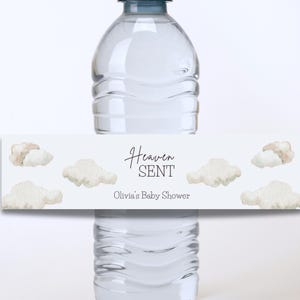 以下が含まれることがあります： 雲と「Heaven Sent」と「Olivia's Baby Shower」の文字が書かれた白いウォーターボトルのラベルです。