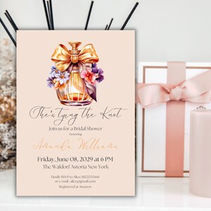 Puede incluir: Una invitación a una despedida de soltera con un fondo rosa y una ilustración de acuarela de un frasco de perfume con un lazo y flores. El texto dice "The's tying the Knot" e incluye el nombre de la novia, la fecha y la hora de la despedida de soltera, y la ubicación.