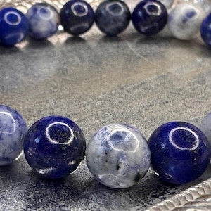 Pode incluir: Um bracelete de pedras preciosas azul e branco com contas redondas. O bracelete é feito de lápis-lazúli e sodalita.