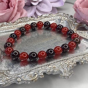May include: A red and black beaded bracelet with a silver tray in the background.