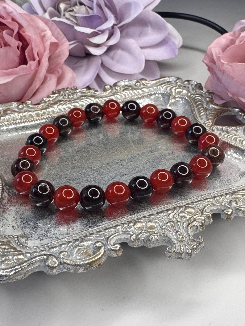 May include: A red and black beaded bracelet with a silver tray in the background.
