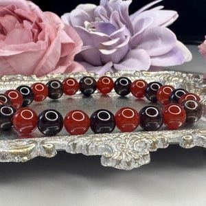 May include: A bracelet made of alternating red carnelian and black onyx beads. The bracelet is displayed on a silver tray.