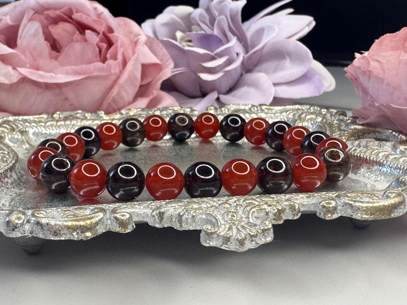 May include: A bracelet made of alternating red carnelian and black onyx beads. The bracelet is displayed on a silver tray.