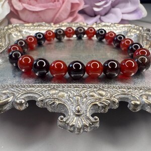 May include: A red and black gemstone bracelet with alternating beads. The bracelet is on a silver tray.
