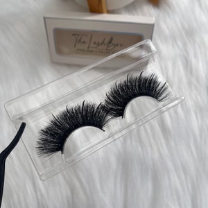 Puede incluir: Dos pares de pestañas postizas negras en un estuche de plástico transparente. Las pestañas son largas y llenas, con un look dramático.