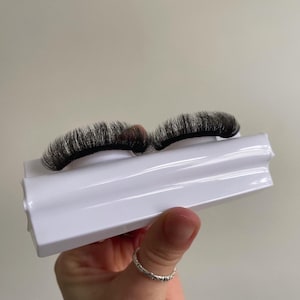 Könnte beinhalten: Zwei Paar schwarze falsche Wimpern auf einem weißen Kunststoff-Wimpernapplikator.