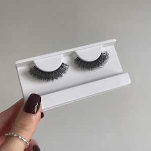 May include: Two pairs of false eyelashes on a white card. The eyelashes are black and have a natural, wispy look.
