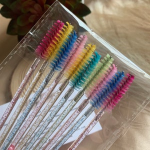 May include: A set of 12 colorful lash wands with glitter-covered handles. The wands are packaged in a clear plastic bag.