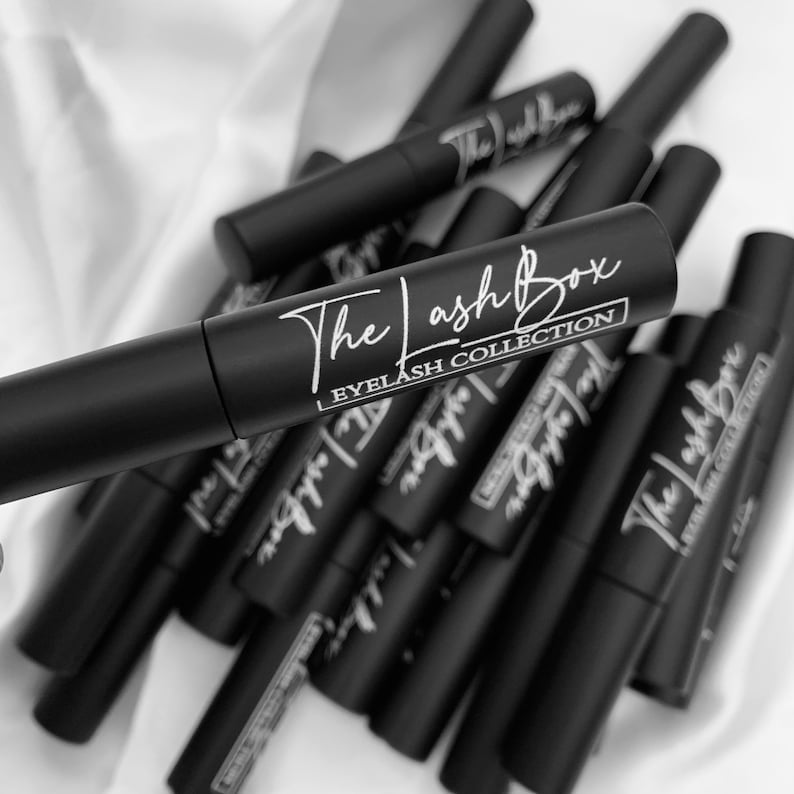 May include: A close-up of a pile of black mascara tubes with white text that reads "The Lash Box Eyelash Collection".