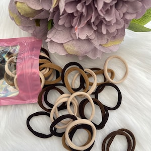 May include: A close-up of a pile of brown and beige hair ties. The hair ties are in a plastic bag with a pink background.