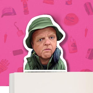 Può includere: Primo piano di un uomo con un cappello verde e una giacca verde. Sta guardando la telecamera con un'espressione seria. Indossa delle cuffie intorno al collo.
