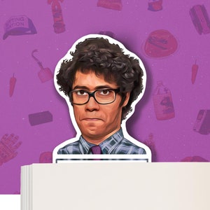 Puede incluir: Un marcapáginas con una ilustración de dibujos animados de un hombre con el pelo castaño rizado, gafas, una camisa a cuadros azul y blanca y una corbata azul oscuro. El marcapáginas está encima de una pila de papel blanco.