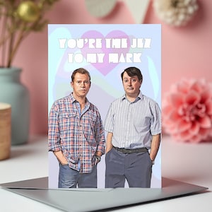 Peut inclure: Carte de vœux avec une illustration de deux hommes. Le texte "YOU'RE THE JEZ TO MY MARK" est écrit en blanc. Le fond est bleu clair avec un cœur rose.
