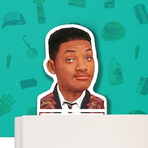 May include: A bookmark featuring a cartoon illustration of Will Smith, with a red, yellow, and green patterned jacket, a white shirt, and a black tie. The bookmark is placed on top of a stack of white paper.
