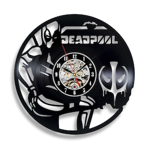 Può includere: Orologio in vinile nero con una silhouette di Deadpool e la scritta "DEADPOOL" in lettere bianche. Il quadrante dell'orologio è visibile con numeri neri e una lancetta dell'orologio argentata.
